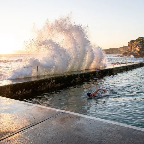 Swimmer slicing through calm water beside a breaking ocean wave
