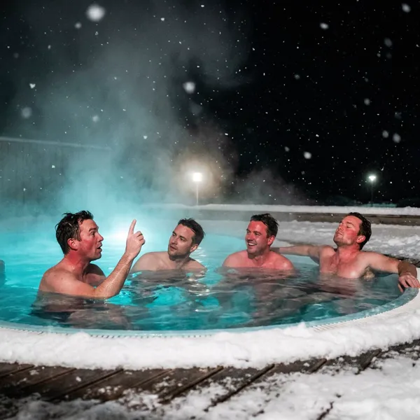 Four men relaxing in an outdoor geothermal hot pot in winter